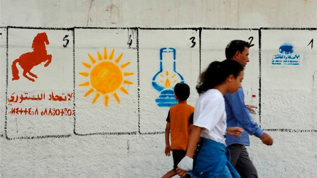 Una familia marroquí camina junto a las pinturas electorales que representan los logotipos de los partidos políticos para las elecciones municipales del 8 de septiembre en Casablanca